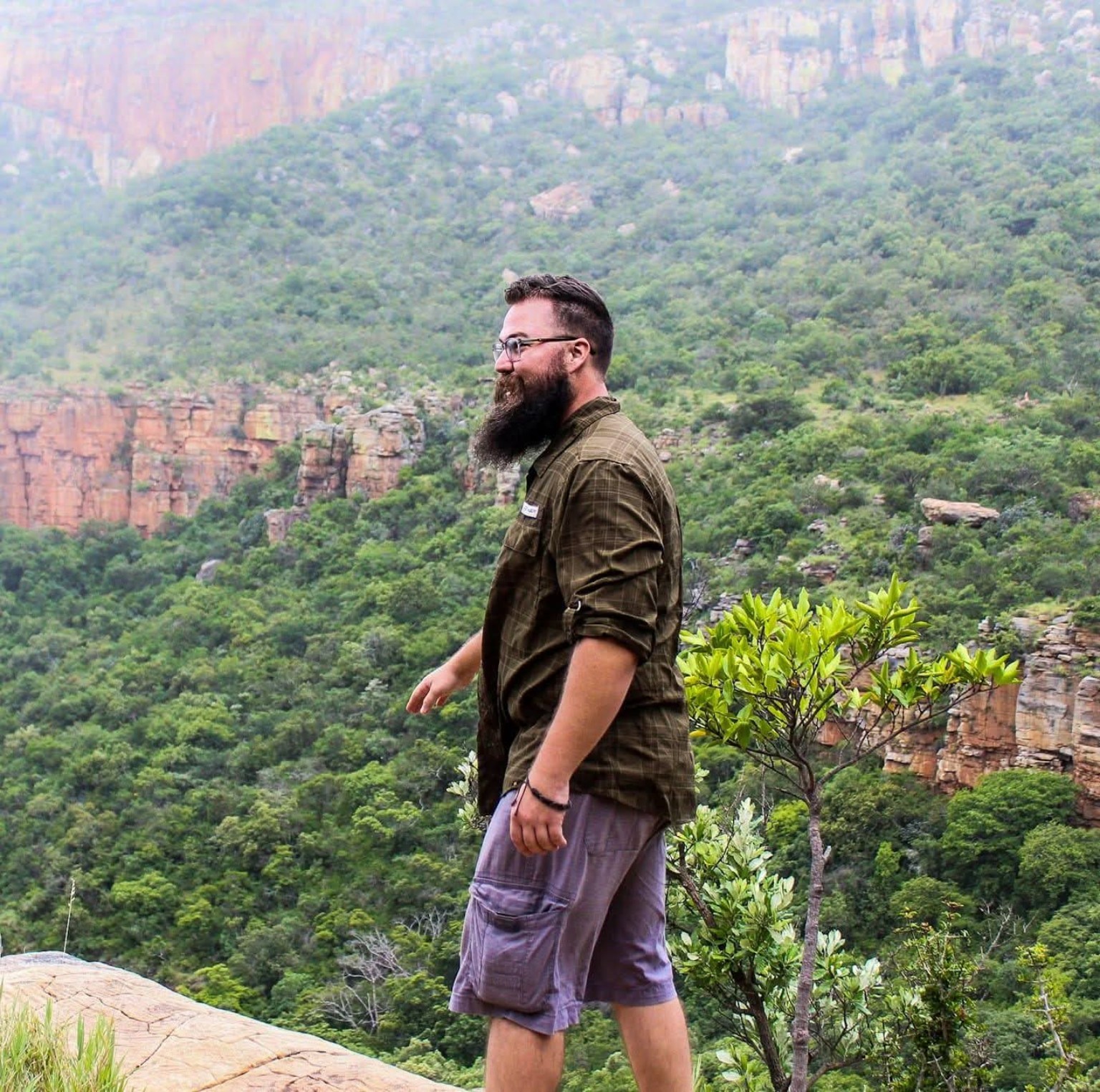 Chris Banotai standing at a mountain overlook surrounded by green cliffs in South Africa.